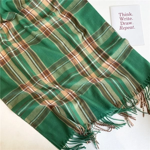 Dettaglio ravvicinato di una sciarpa a quadri verde in finta cashmere con frange morbide