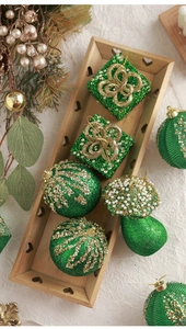 Detail view of dark green flocked Christmas ornaments with gold glitter on wooden tray