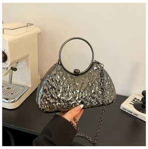 Detail of evening clutch featuring textured metallic surface and round ring handle