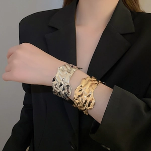 Detail of wide metallic cuff bracelet with wavy lava texture on black suit sleeve