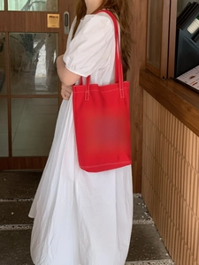 Close-up of red canvas tote bag with white HAPPY letter print worn by a model