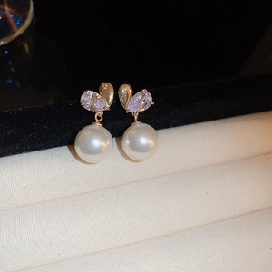 Macro view of gold-plated earring featuring a sparkling zircon heart and white pearl