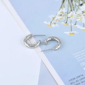 Detailed close-up of silver C-shape earrings with quilted texture on blue floral background