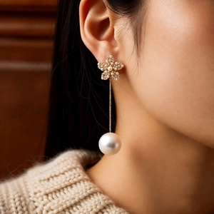Close-up of elegant 18k gold-plated flower stud earrings with long pearl drop pendant