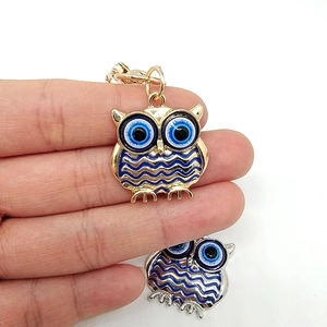 Golden owl keychain pendant with blue evil eye design held in hand for scale