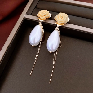 Detail of gold mesh rose earrings featuring drop pearls and long chain tassels