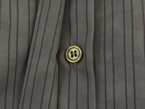 Macro shot of an olive green four-hole button on taupe vertical stripe fabric texture