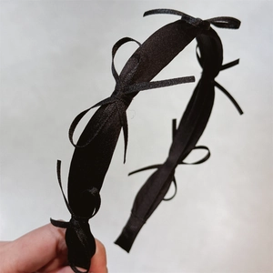 Detailed close-up of a black satin headband featuring multiple elegant bow decorations
