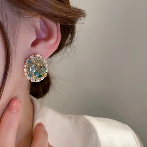 Close-up detail of vintage round stud earrings with crystals and green beads on a model