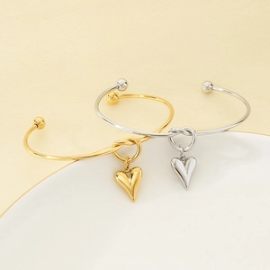 Detailed close-up of gold and silver stainless steel open bangles with heart pendants