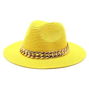 Detail of yellow straw fedora hat featuring a chunky gold chain and textured weave