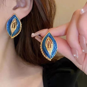 Detailed view of vintage gold-trimmed blue leaf earrings held by fingers for texture