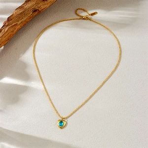 Golden stainless steel heart pendant necklace with blue gem on rustic wood and beige surface