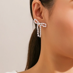 Close-up of bow-shaped pearl earrings made of small white beads on a model