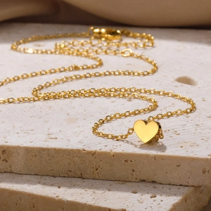 Close-up of golden heart pendant necklace with lobster clasp on travertine stone