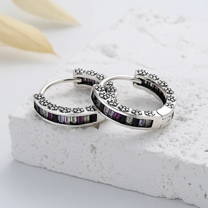 Macro detail of silver hoop earrings with colored zircons and floral relief patterns