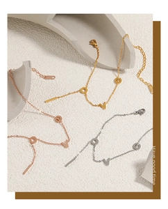 Detailed close-up of gold, rose gold and silver LOVE letter anklets on geometric stone props