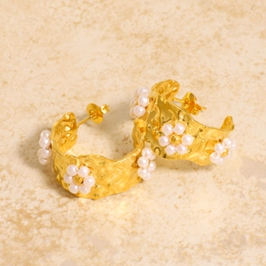 Golden textured C-shape hoop earrings with small pearl flowers on marble surface