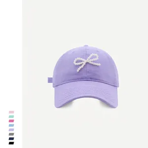 Detailed view of the pearl bow embellishment on a lilac cotton baseball cap crown