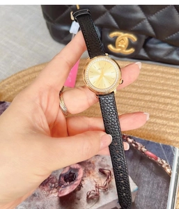 Detailed close-up of a gold quartz watch with a diamond-set bezel and black leather strap