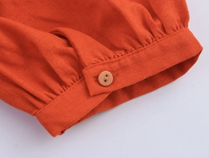 Close-up of orange-red V-neck dress sleeve with fabric texture and button detail