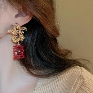 Close-up of gold flower earrings with red Double Happiness pendant on model