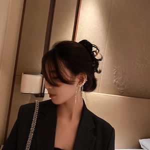 Detail of golden tassel ear cuff with rhinestones worn by a model in warm lighting