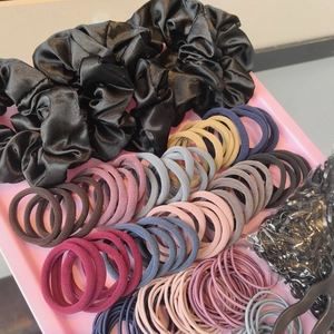 Assorted hair accessories set with silk scrunchies and elastic ties on a pink tray