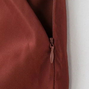 Close-up of rust red satin skirt with invisible zipper and smooth fabric texture