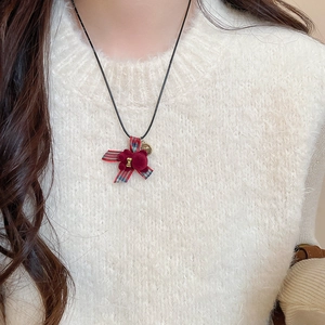 Dettaglio del ciondolo a forma di orsetto bordeaux con fiocco scozzese su maglione bianco