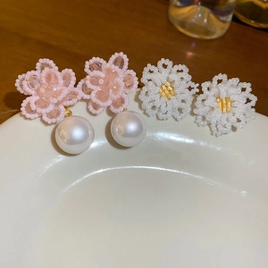 Macro detail of handmade beaded flower earrings with white pearls on a ceramic dish