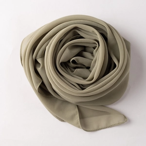 Close-up of sage green chiffon hijab scarf folded into a rose shape on a white background