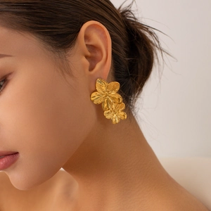 Detailed view of large gold floral earrings worn by a model in soft lighting