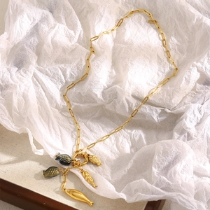 Detail of 18K gold-plated paperclip chain necklace with textured fish charms on white paper