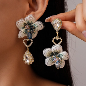 Détail macro de boucles d'oreilles fleurs en tissu asymétriques et gouttes de cristal