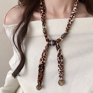 Leopard print fabric necklace with Saturn logo and beaded charms on a beige sweater
