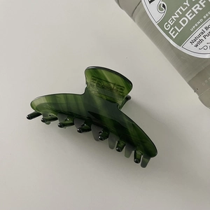 Macro detail of a dark green translucent acetic acid hair claw clip for hair styling