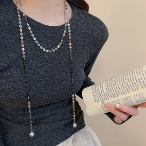 Long silver chain necklace with black beads and pearls shown on a model for layered look