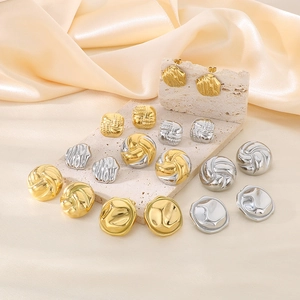 Macro shot of irregular pleated gold and silver earrings on a textured stone display