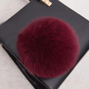 Détail macro d'un pompon en fourrure véritable bordeaux sur un sac en cuir noir