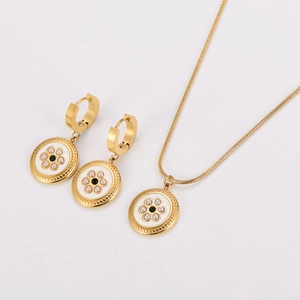 Close-up of golden necklace and earrings set with white shell flowers and emerald green stones