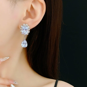 Detail of silver drop earrings with zircons worn by a model against black background