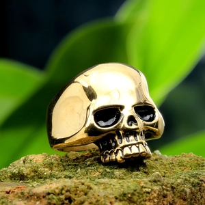 Macro detail of a golden skull punk ring with vintage finish on a mossy stone background