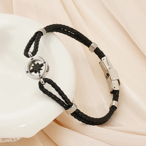 Detail of a black braided leather bracelet with silver compass charm on satin fabric