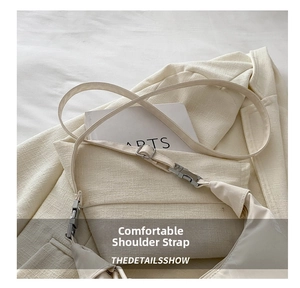 Close-up of minimalist cream crossbody bag with industrial buckle on neutral blazer