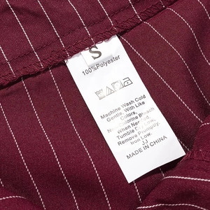 Macro shot of product care label on burgundy pinstripe fabric showing 100% polyester material