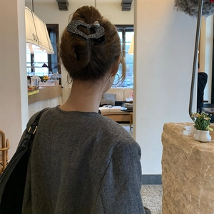 Dettaglio di un fermaglio per capelli grigio glitterato a forma di cuore con perla su donna