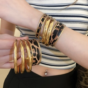 Detail view of stacked leopard print leather cuff and golden metallic bangles on wrist