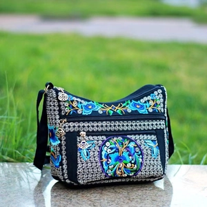 Detailed close-up of intricate floral embroidery on black canvas crossbody bag zippers