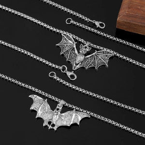 Close-up of two silver bat-shaped pendants with detailed textures on black background